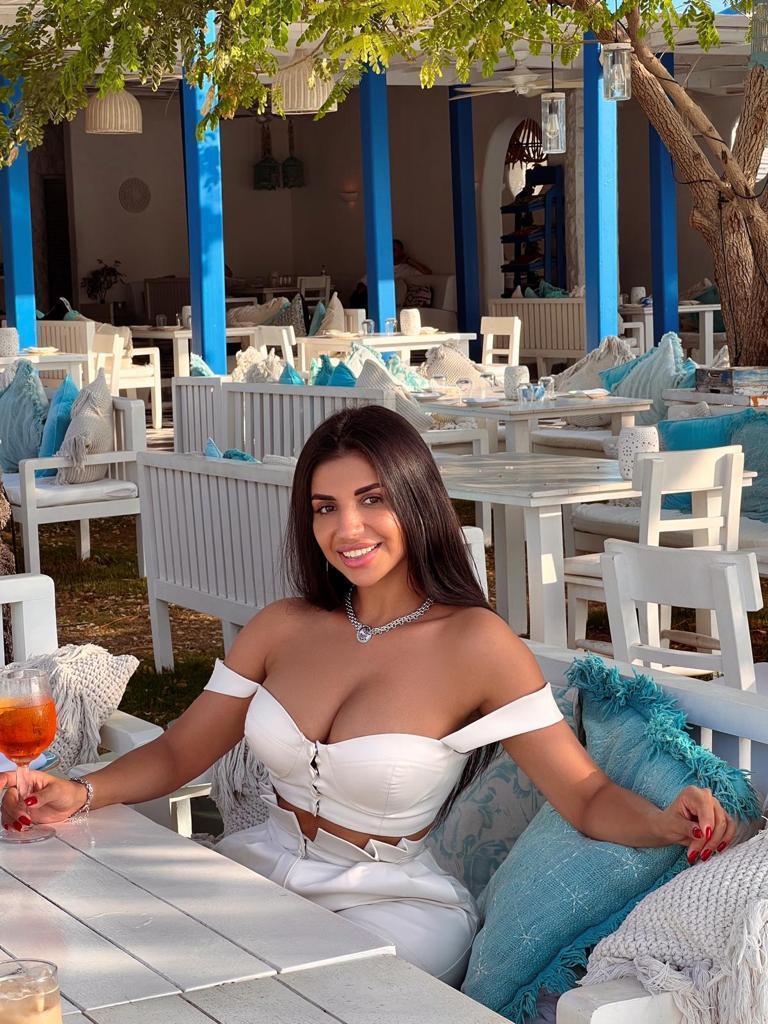 Samantha sitting at a table while smiling and wearing a white top. 