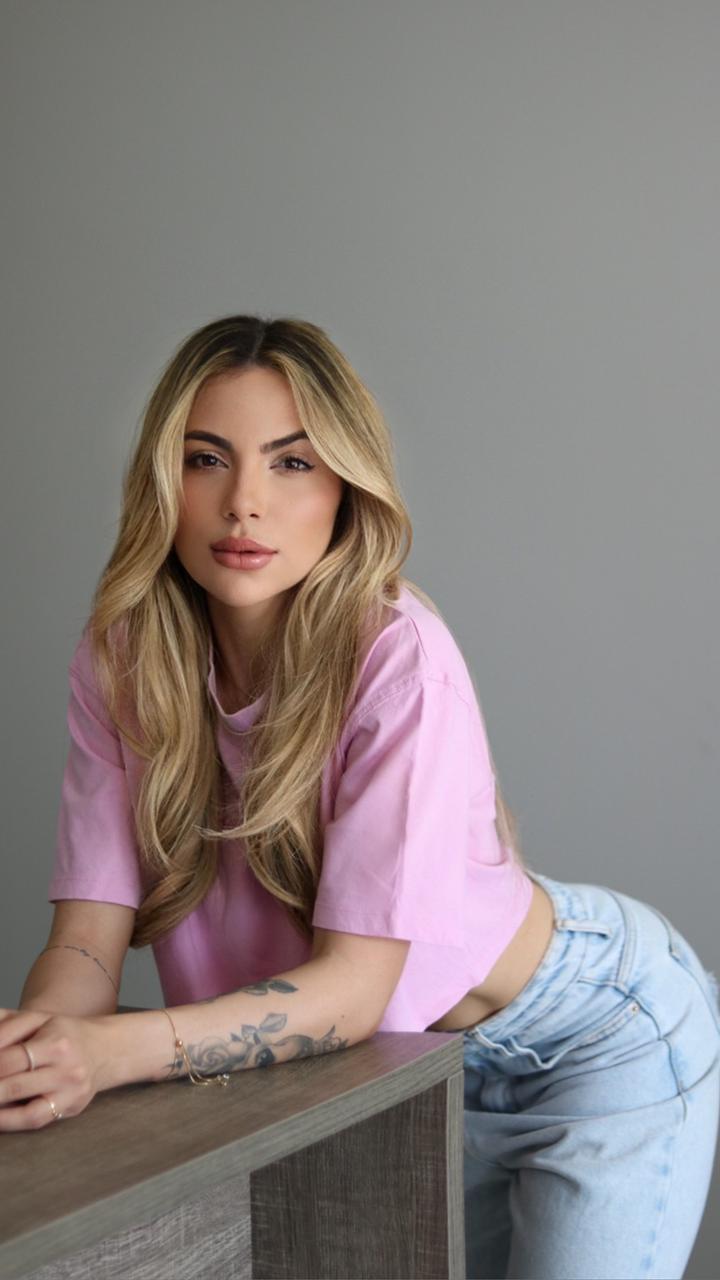 Mari leaning over a desk while wearing jeans and a pink top 