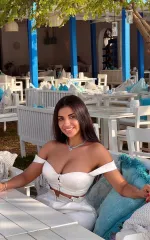 Samantha sitting at a table while smiling and wearing a white top. 