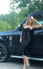 Alice standing next to a black rover in a black dress 