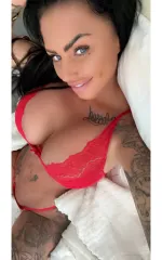 Kerry taking a selfie in bed while wearing a red set of lingerie, showing off her breasts 